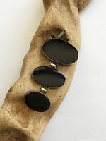 Front view of pendant on driftwood showing three oval black cabochons in silver settings
