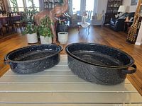 Two black speckled enamel oval roasting pans side by side showing size difference