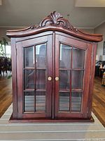 Front view of cabinet with doors closed showing glass panes and carved crest