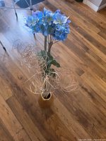 Full view of arrangement showing blue hydrangea, purple chrysanthemum and rattan sprays in brown vase