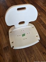 Front angled view of white plastic shower chair showing seat perforations and backrest handle