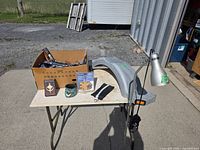 Overall lot view with fender, lamp, cardboard box and small items on table