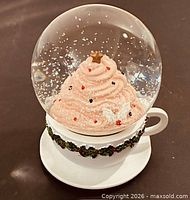 Front view of snow globe showing cupcake and holly-trimmed teacup base