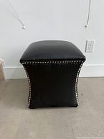 Front view of faux leather storage ottoman showing nailhead trim and tapered sides