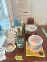 Group of assorted boxed and unboxed candles with decorative holder displayed on tabletop