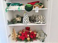 Shelved lot showing stockings, garland, silver ornament tree, JOY holders, wooden tree, poinsettia centerpiece and glass gift box light