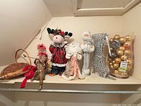 Shelf with all holiday items: basket, cherub statue, reindeer doll, two Santa figurines, silver stocking, glass vase of gold ornaments