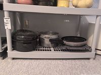 Shelf holding black speckled enamel roasting pan with lid, two nested aluminium saucepans and two nested non-stick frypans