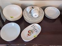 Mixed china stacks of plates, bowls, cups and oval platter on sideboard