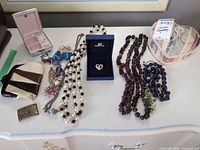 Entire lot displayed on table showing pendants, necklaces, earrings, brooch, bracelet, belt buckle, coin purse and trinket box