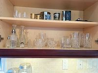 Cabinet shelf showing decanters, glasses, creamer, sugar bowl, shakers