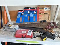 Lot overview showing air compressor in blister pack, three Clamp & Sand packs, Contractor sanding sheet pack, two hand saws, Hilti case, tape measures