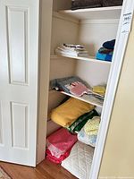 Linen closet shelves holding folded towels, table linens, crochet items, blankets, mattress pad