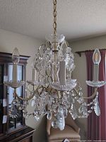Full view of chandelier unlit, showing brass arms, crystal drops, five candle sockets