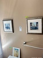 Two silver framed prints hung on wall and third print leaning below