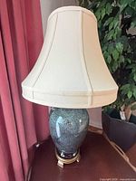 Front view of speckled teal ceramic table lamp with cream bell shade on brass-tone base