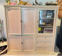Front view of armoire cabinet showing paneled doors, glass display door, drawers, hardware and finish