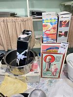 Overall lot showing boxed Meliconi Gradosa grater, Meliconi sugar dispenser, Hamilton Beach DrinkMaster box, stainless pot, Braun box visible