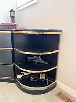 Corner shelf front view showing black finish, gold trim, three shelves