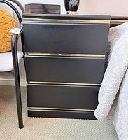 Front view of black nightstand, drawers closed, gold trim visible