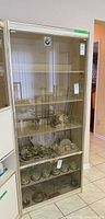 Front view of tall cream laminate cabinet with glass doors and contents inside