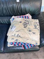 Stack of two abstract brushstroke pillows with grid pillow partly visible, blanket folded on top