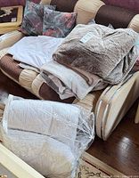 Overall view of pillows, blankets, and packaged comforter on loveseat