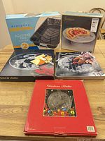 All five boxed items grouped: roasting pan, cake stand, two black boxed platters, red boxed Christmas platter