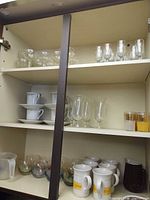 Cabinet shelves showing full assortment of glassware, porcelain cups, saucers, mugs and pitchers