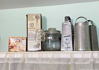 Full lot on shelf showing boxed items, glass pot and three graters