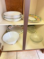 Cabinet shelves showing stack of ceramic bowls, hand-painted platter, large white bowl, ceramic plate and clear glass bowls/dishes