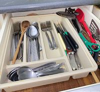 Drawer tray containing mixed stainless flatware, serving utensils, can opener, shears, spatula