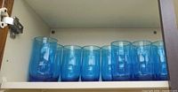 Eight blue drinking glasses lined in cabinet