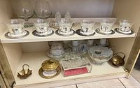 Upper shelf showing six glass cups in silver holders with saucers, two brandy snifters, crystal salt and pepper shakers