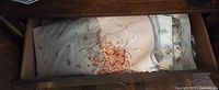 Drawer view of folded embroidered cream tablecloth with orange floral bouquet