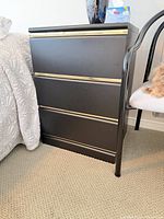 Front view of black three-drawer nightstand beside bed