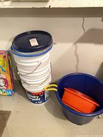 Stacked white buckets with blue lids beside blue tub containing orange basin