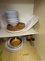 Stack of grey bowls, mustard plates, white oval platter on shelf