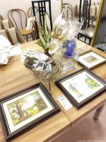 All items on table: two framed prints, glass bowl on stand with potpourri, blue glass dish, faux floral arrangement