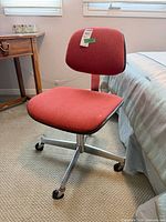 Full front view of red swivel office chair beside bed