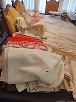Stack of assorted linens: white and ivory cloths, lace pieces, red gingham fruit towel