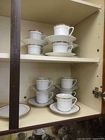 Cabinet shelf showing multiple white porcelain tea cups stacked on saucers