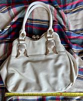 Front view of beige faux leather handbag showing handles, hardware, texture