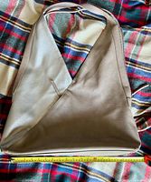 Full view of taupe handbag on plaid background with tape measure showing width