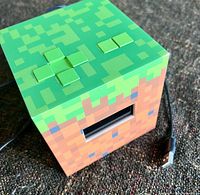 Front angled view showing pixelated dirt/grass design, LCD screen, attached USB cable