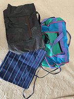 Group shot of three bags: floral tote, teal duffel, striped bag