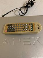 Remote resting on top of Apex lid, showing logo embossing and integrated power cord