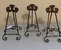 Three ornate cast brass display stands on table
