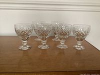 Six clear cut crystal water goblets on wooden surface
