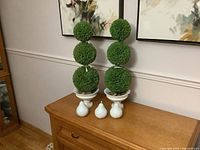 Overall view of two topiaries with three pear figurines on wooden surface